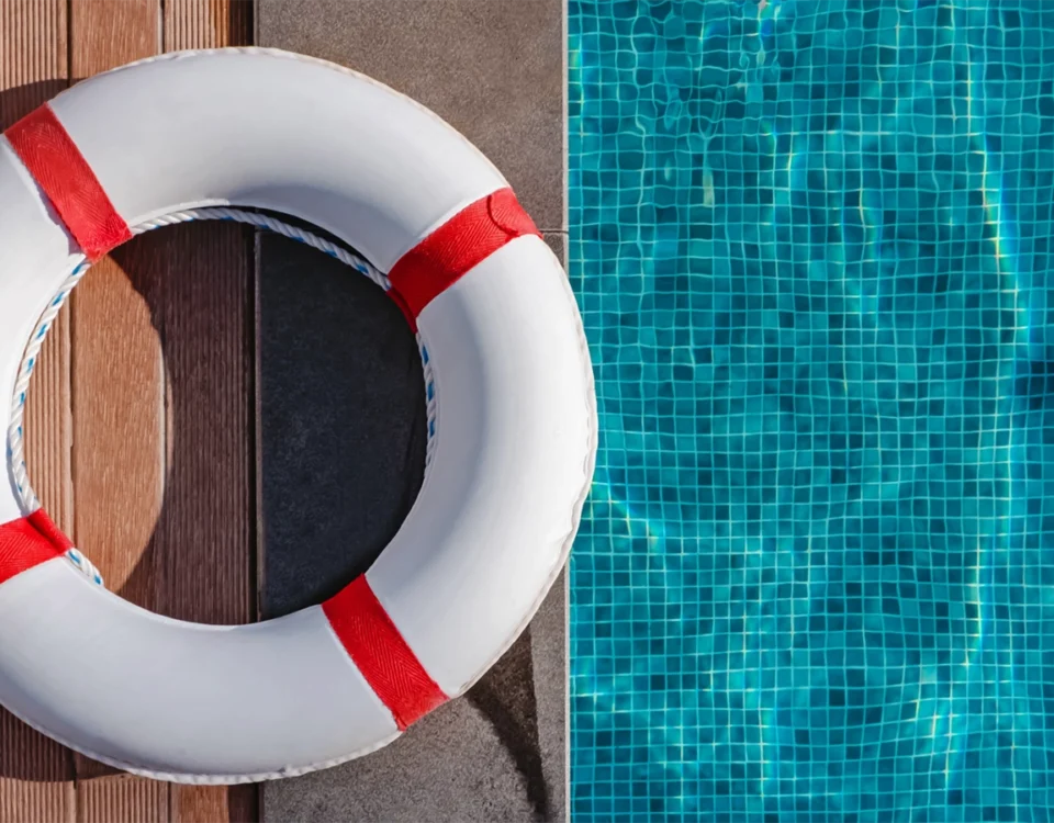 White and red life ring lying on wooden deck beside a tiled swimming pool
